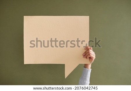 Young anonymous woman holding one empty beige square speech bubble in hand on green background. Blank paper card layout with copy space for message, quote, inspiration, opinion or vote. Royalty-Free Stock Photo #2076042745