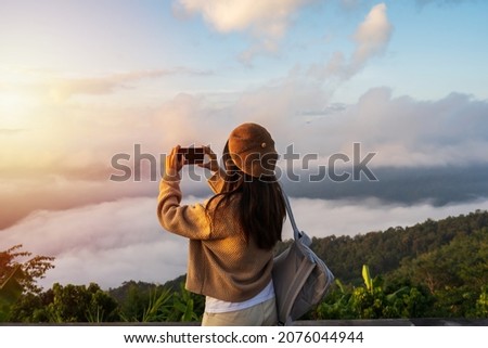 Young woman traveler taking photo with smart phone at sea of mist and sunrise over the mountain Royalty-Free Stock Photo #2076044944