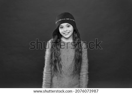 Fashionable wear for chilly trips. Happy child in fashionable winter style red background. Small girl smile in fashionable knitted hat. Fashionable and warm essentials for cold weather adventures