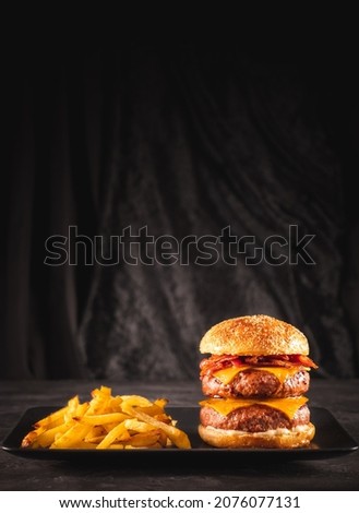 Double beef and bacon burger with cheddar cheese and chips on a black plate on a dark table, ready to eat. Photo with copy space. 