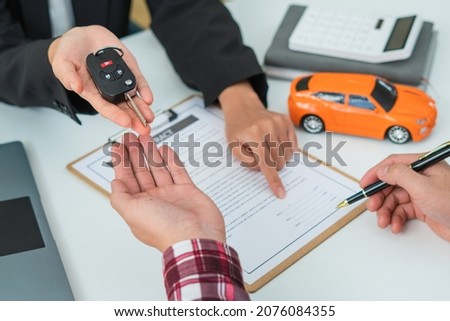 Sale agent handed over the rental car key to the customer who signed the contract and the terms of the agreement on the document, Car rental service concept.