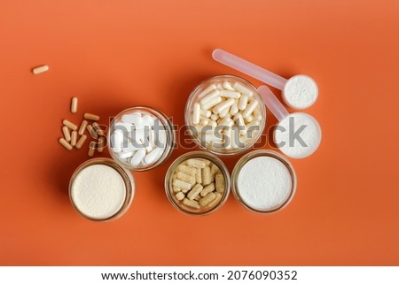 Nutrition supplements, glass of water and different vitamins such as vitamin C, magnesium, vitamin A, protein, electrolytes and collagen peptides in beautiful composition on orange bright background. Royalty-Free Stock Photo #2076090352