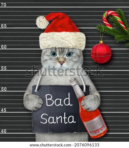 An ashen cat in a red hat with a sign around its neck that says Bad Santa holds a bottle of wine in jail. Black lineup background.