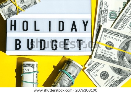 Lightbox board with word HOLIDAY BUDGET on yellow background around dollar banknotes. Money, Business, finance, investment, saving. Cash bill. Business budget of wealth and prosperity finance. Passive