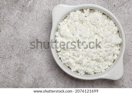 Fresh dairy farm product cottage cheese in ceramic bowl on a concrete background on table close-up top view. Healthy food containing calcium, lactose, protein, methionine, amino acid, vitamin, casein. Royalty-Free Stock Photo #2076121699