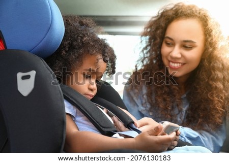 African-American woman and her little daughter watching cartoons in car safety seat