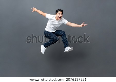 Young handsome energetic Asian man jumping with hands outstratched in isolated studio gray background