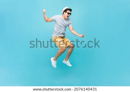 Young Asian tourist man jumping and yelling in light blue color studio isolated background