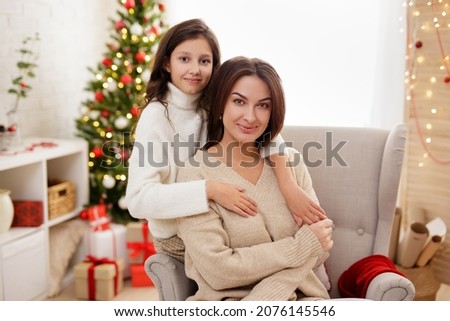 family and Christmas concept - portrait of happy mother and cute daughter sitting in decorated room with Christmas tree