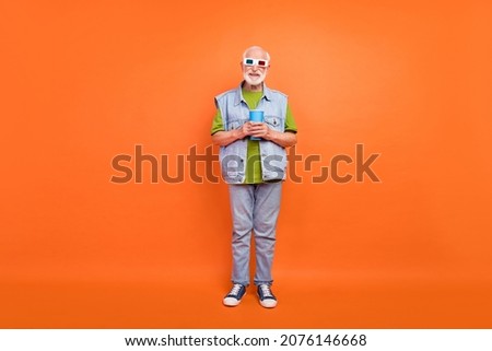 Photo of pretty cute man pensioner dressed retro denim vest 3d eyewear smiling drinking beverage isolated orange color background
