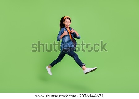Photo of sweet funny preteen girl dressed jeans shirt walking showing thumbs up jumping high smiling isolated green color background