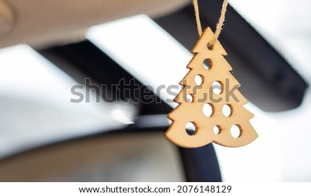 a snowflake, fir tree and deer toy hanging in a modern car on rear view mirror.part of the image is blurred.details of modern hybrid car.christmas mood, winter holidays eco wooden toys hanging.