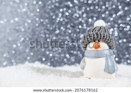 Christmas panorama background. Happy cute penguin in a winter hat on snowdrifts in the light of a lantern at night with hard shadows on the snow, and night bokeh. Christmas or New Year concept