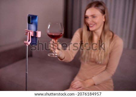 Happy young smiling caucasian woman making video call with smartphone at living room. Best friends drinking red wine and toasting. Video conference party online meeting with family