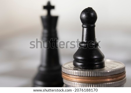 A pawn figure playing chess on a stack of coins on the background of a king figure.