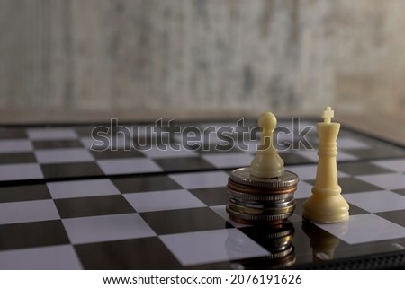 A white pawn figure plays chess on a stack of coins against the background of a king figure.