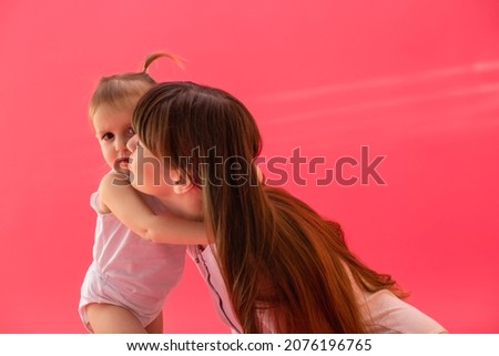 blonde mom kisses little daughter on the cheek on a pink background