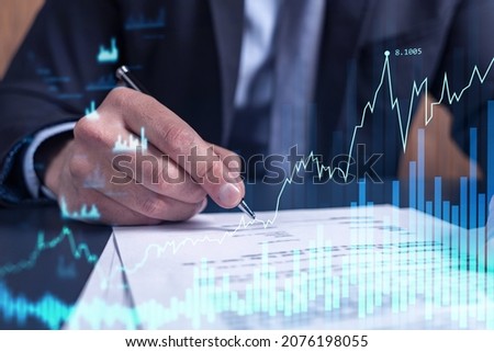 A client in formal wear is signing the contract to invest money in stock market. Internet trading and wealth management concept. Forex and financial hologram chart over the desk. Royalty-Free Stock Photo #2076198055