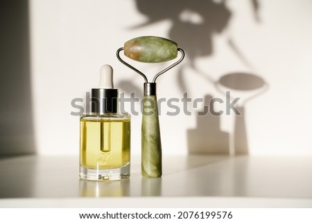 green jade roller and yellow face oil on white background with plant eucalyptus shadows. Copy space self care advertisement