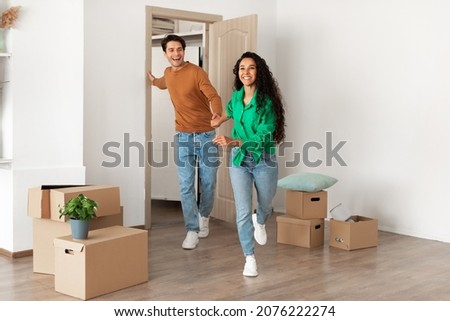 Happy young family running in new apartment, young couple bought new house. Smiling happy guy and lady walking into big modern home, holding hands. Real estate dwelling, loan and mortgage concept Royalty-Free Stock Photo #2076222274