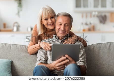 Cheerful Mature Couple Using Digital Tablet Computer Watching Movie Together Sitting On Sofa At Home. Senior Spouses Browsing Internet Using Gadget. Technology, Retirement Lifestyle Concept Royalty-Free Stock Photo #2076222385