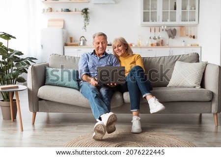 Senior Spouses Using Laptop Watching Movie Together Sitting On Couch At Home. Older Couple Browsing Internet On Computer Reading Online News On Weekend. Technology And Gadgets Royalty-Free Stock Photo #2076222445