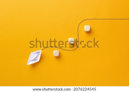 Origami paper boat passes through the wooden cube barriers. To overcome obstacles or barriers in business or education concept. Royalty-Free Stock Photo #2076224545