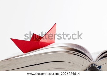 Origami red paper boat floating on the pages of a book on white background. Learning, education, reading, knowledge or conquering adversity concept. Royalty-Free Stock Photo #2076224614