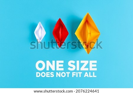 Difference, variety, plurality or diversity concept. Three paper boats with different size and colors on blue background with the text one size does not fit all. Royalty-Free Stock Photo #2076224641