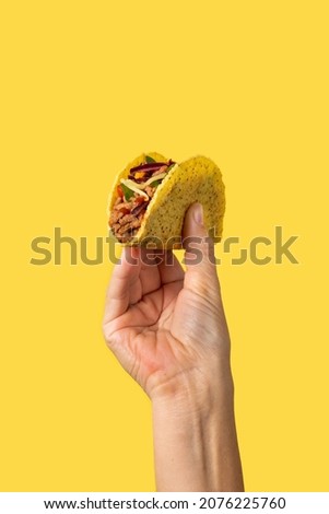 Hand holding a Mexican taco on yellow background Royalty-Free Stock Photo #2076225760