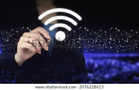 Business networking connection concept. Hand holding digital graphic pen and drawing digital hologram Wi Fi sign on city dark blurred background. Wi Fi wireless concept