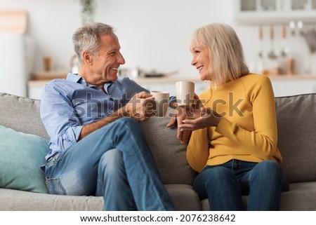 Cheerful Mature Couple Drinking Tea And Talking Sitting On Sofa At Home. Retired Senior Spouses Holding Cups Of Coffee Enjoying Conversation On Weekend. Retirement Lifestyle, Happy Marriage Royalty-Free Stock Photo #2076238642