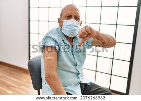 Mature hispanic man with grey hair getting vaccinated with angry face, negative sign showing dislike with thumbs down, rejection concept 