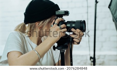 Photo of a Professional Camera Capturing a Picture. Young Female Photographer Wearing Rings and Capturing a Photograph while Wearing a Hat in a Modern and Industrial Looking Photo Studio.