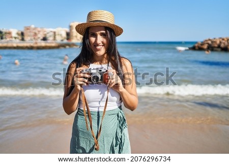 Young hispanic woman smiling confident using camera at seaside