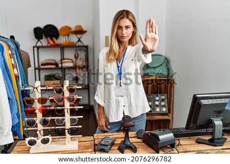 Blonde beautiful young woman working as manager at retail boutique doing stop sing with palm of the hand. warning expression with negative and serious gesture on the face. 