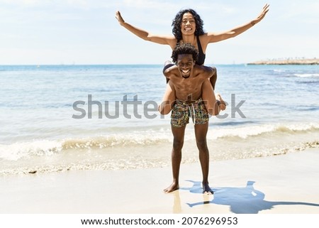 Young african american man holding girlfriend on his back at the beach.