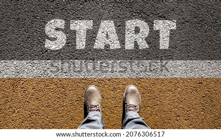 The word Start on the asphalt in front of your feet in boots. View from above. Starting line. The concept of beginnings, choice, business.