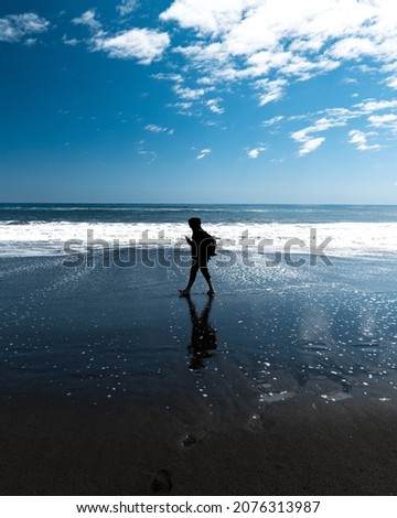 Silhouette of a young man walking barefoot looking at his phone on the shore of the beach in pichilemu.