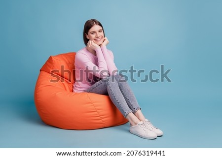 Full length profile side photo of young girl sitting in beanbag chair isolated on blue colored background