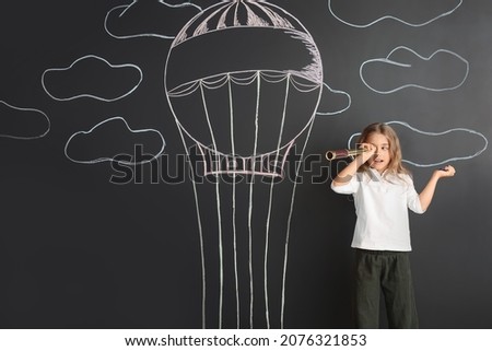 Cute little girl watching in spyglass on black wall with drawn hot air balloon