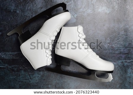 White ice skates for figure skating on a dark surface. Winter sport and recreation concept. Top view, flat lay.