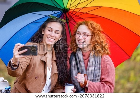 Cheerful female couple taking selfie under rainbow color umbrella 