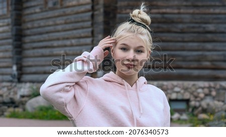 Portrait of a young Russian blonde straightens her hair on a blurred background of an old wooden house