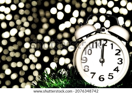 New Year at Midnight. Clock at twelve o'clock with bright holiday lights in the background.
