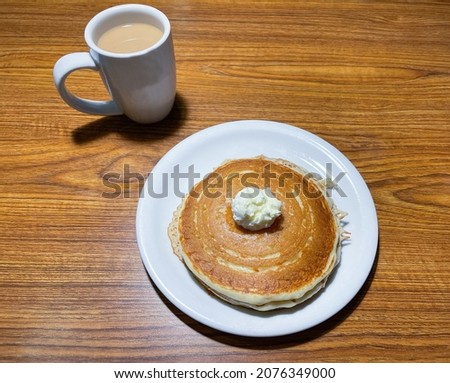 A plate with pancakes with butter on top and a cup of coffee with cream.
