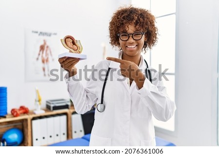 Young african american doctor woman holding anatomical model of female uterus with fetus smiling happy pointing with hand and finger 