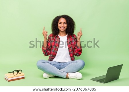 Full body photo of young african girl sit floor indciate figner empty space ads laptop choice isolated over green color background
