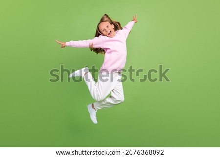 Full size photo of cool little blond girl jump wear sweatshirt trousers sneakers isolated on green background