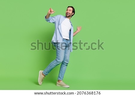 Full size photo of joyful millennial guy move look empty space wear shirt jeans shoes isolated on green color background